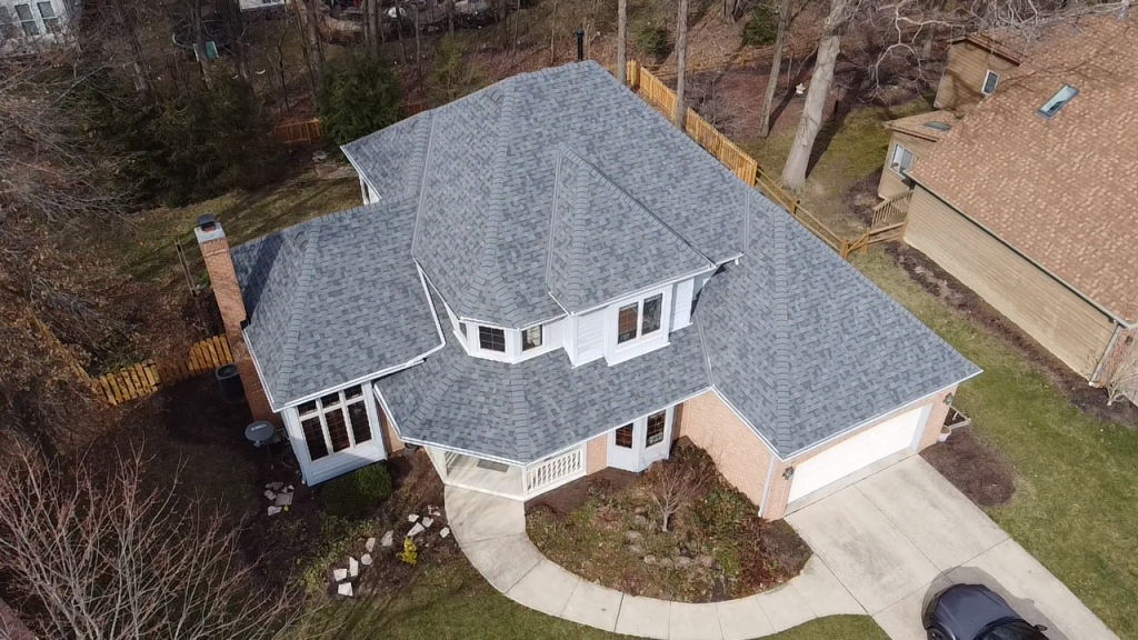 Aerial view of a two-story residential house with gray shingles, a driveway, and surrounding trees. roofing contractor new albany oh 