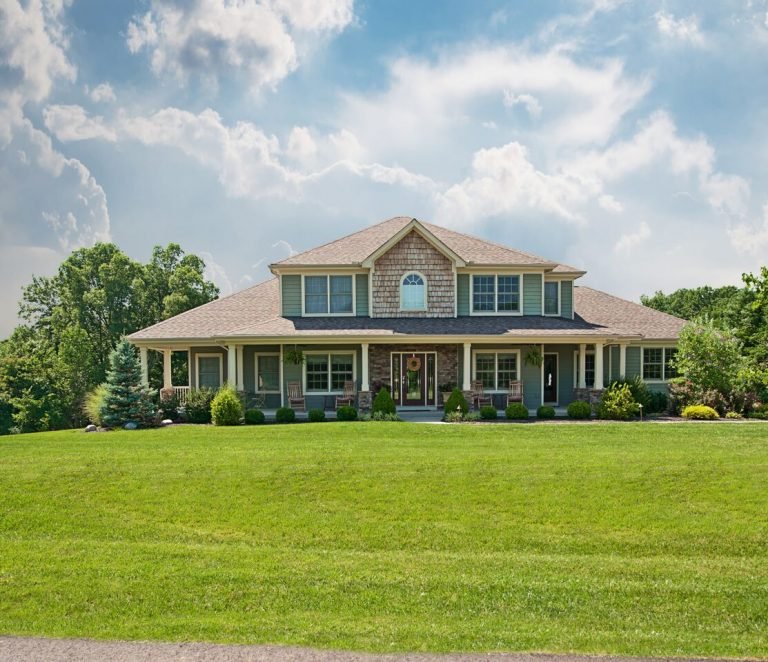 A large two-story house with a green lawn, landscaping, and a blue sky with scattered clouds.