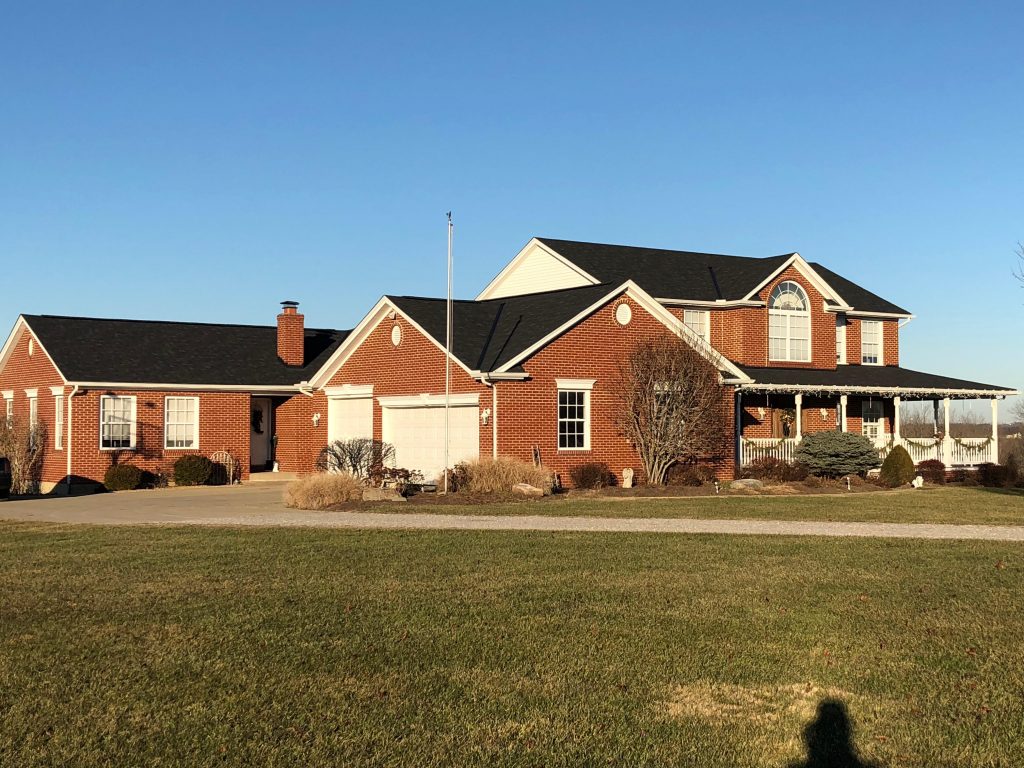 A large, red-brick single-family home with multiple windows, a chimney, and an expansive lawn, captured under a clear sky during daytime.