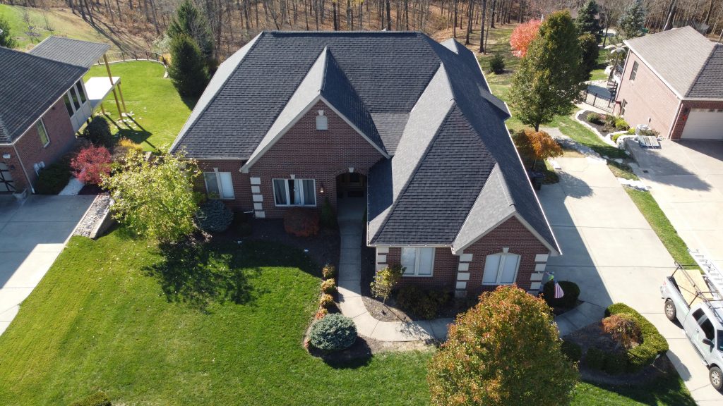 Aerial view of a brick suburban house with a well-manicured lawn and adjacent driveway in a residential area.