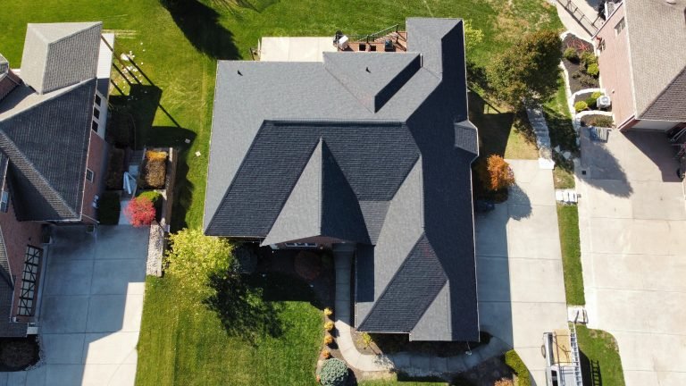 An aerial view of a residential area showcasing the geometric rooftop of a house surrounded by well-kept lawns and driveways.