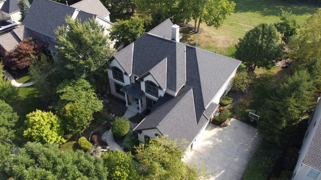 An aerial view of a large two-story house with a grey roof, surrounded by greenery and a driveway with two cars.