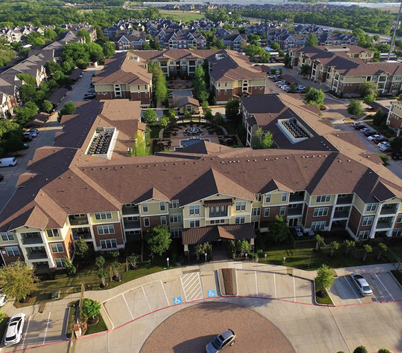 An aerial view of a residential complex with multi-story buildings, parking spaces, and green surroundings.