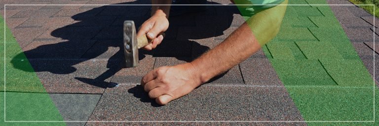 A person is using a hammer to install or repair asphalt roofing shingles on a roof.