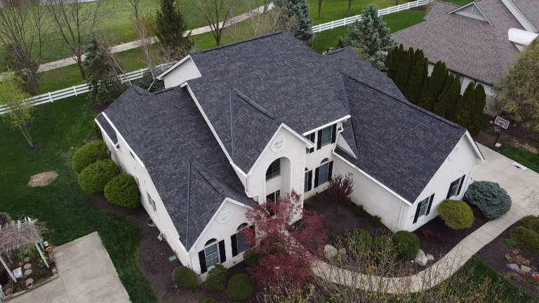An aerial view of a large two-story house with a gray roof, surrounded by a well-manicured lawn and landscaping.