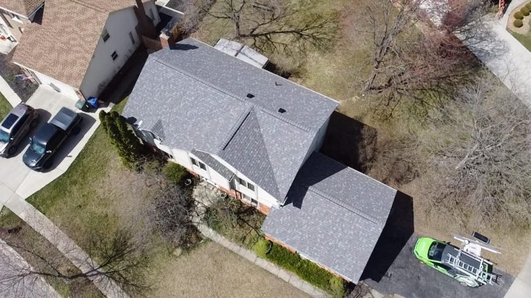 An aerial view of a residential property with a house, driveway, and a vehicle parked alongside.