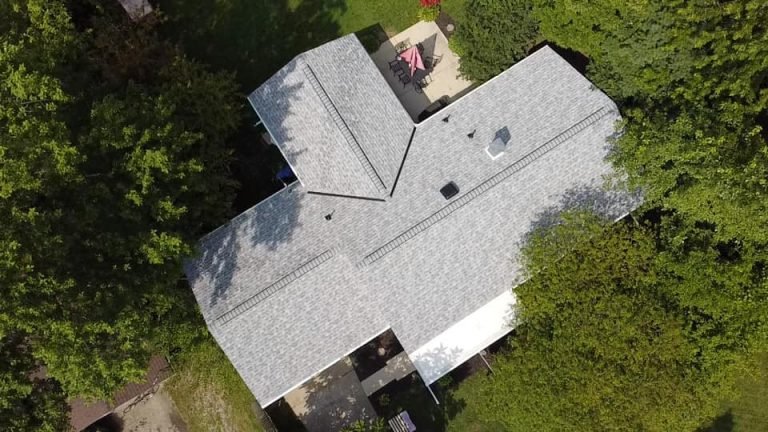 Aerial view of a residential home with a grey shingled roof surrounded by lush greenery.