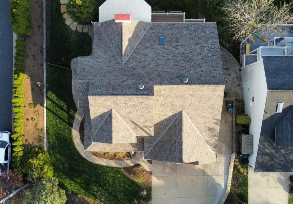 An aerial view of a residential house with a complex roof design and a driveway with a parked car.