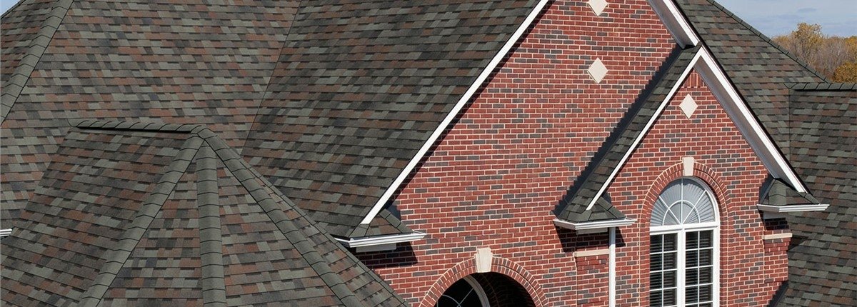 The image shows the detailed roofline of a brick residential house with multiple gabled sections and shingle roofing.