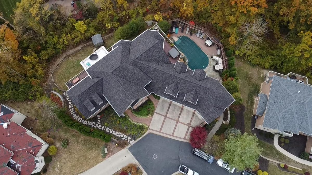 An aerial view of a large house with a pool and a patio surrounded by autumn-colored trees.