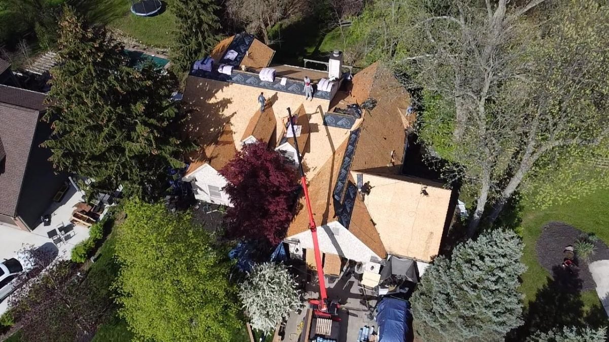 Aerial view of a residential roofing construction with workers and materials on a bright day.