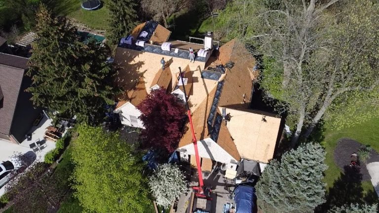 Aerial view of a residential roofing construction with workers and materials on a bright day.