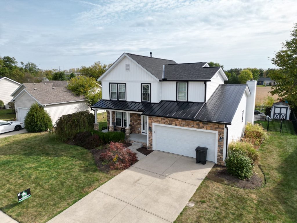 A two-story suburban home with a black roof and an attached garage, surrounded by a well-manicured lawn and neighboring houses.