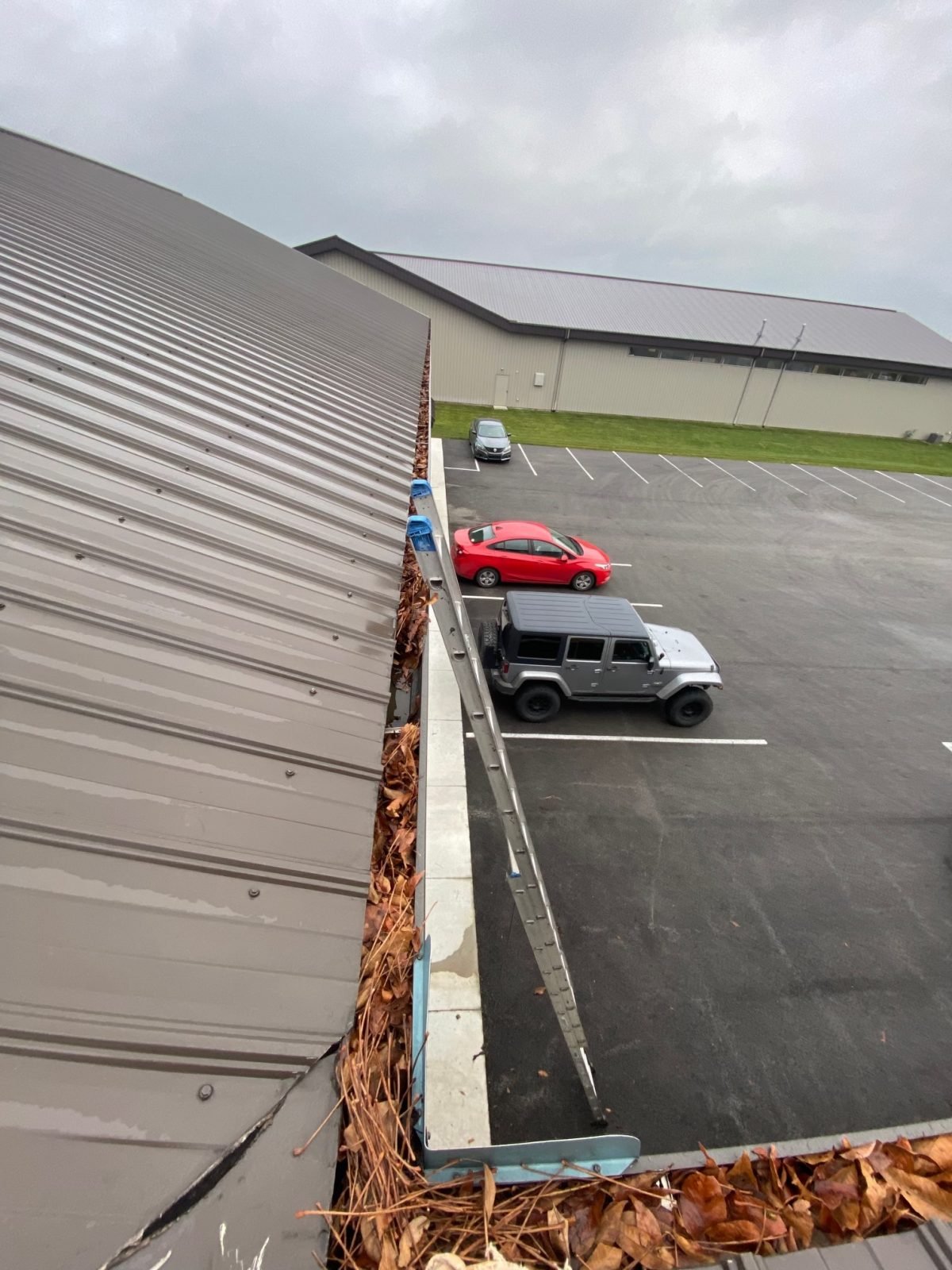 An elevated view of a parking lot with a few cars and fallen leaves near a building's rooftop edge for Gutter instillation Dublin