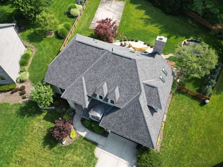 An aerial view of a residential house with a grey roof, surrounded by a well-maintained lawn and landscaping.