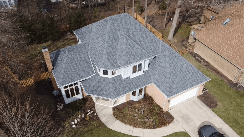 Aerial view of a two-story residential house with gray shingles, a driveway, and surrounding trees. roofing contractor new albany oh