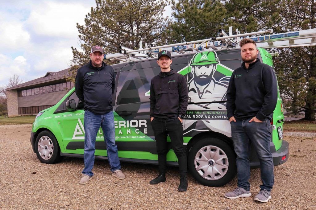 Three exterior alliance contractors are standing beside a branded service van with graphics, possibly representing a roofing company. Interested in top-quality Residential Roofing In Dublin, Ohio? we offers the best storm roofing services in Dublin OH. Click here!